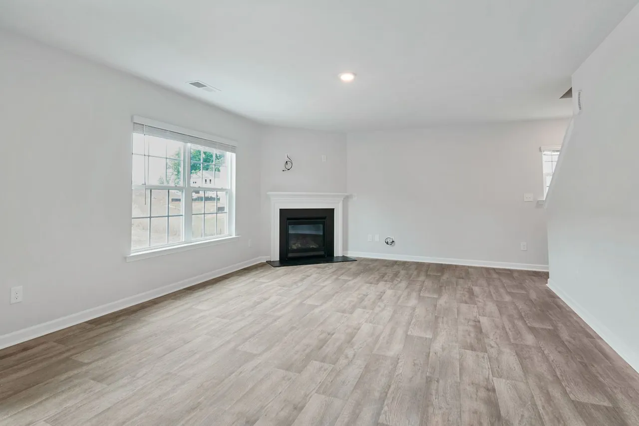 An empty, sunlit living room with wood flooring and a fireplace